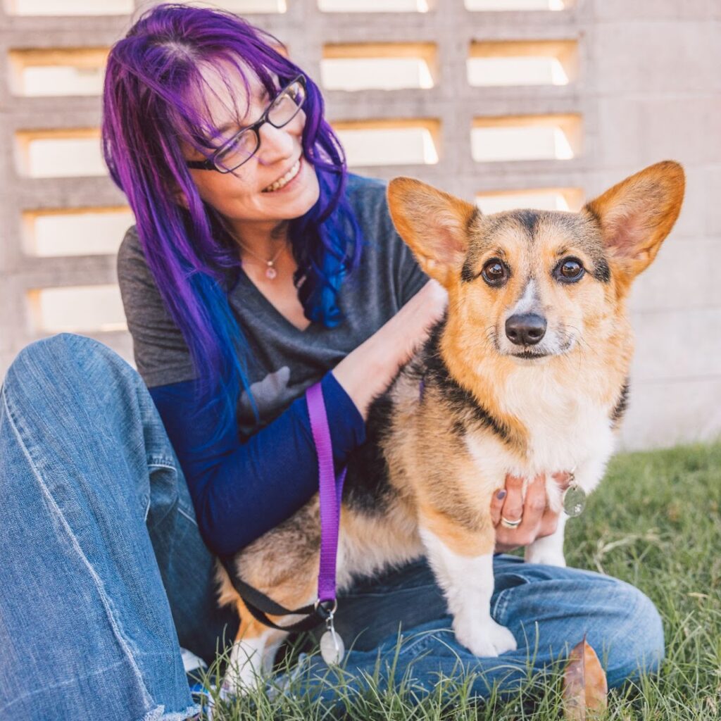 Nicole smiling at a corgi in an outdoor setting, both appearing happy and engaged.